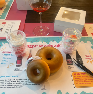 Blank donut sculptures ready to be decorated on a table with toppings and a glass of rose wine. 
